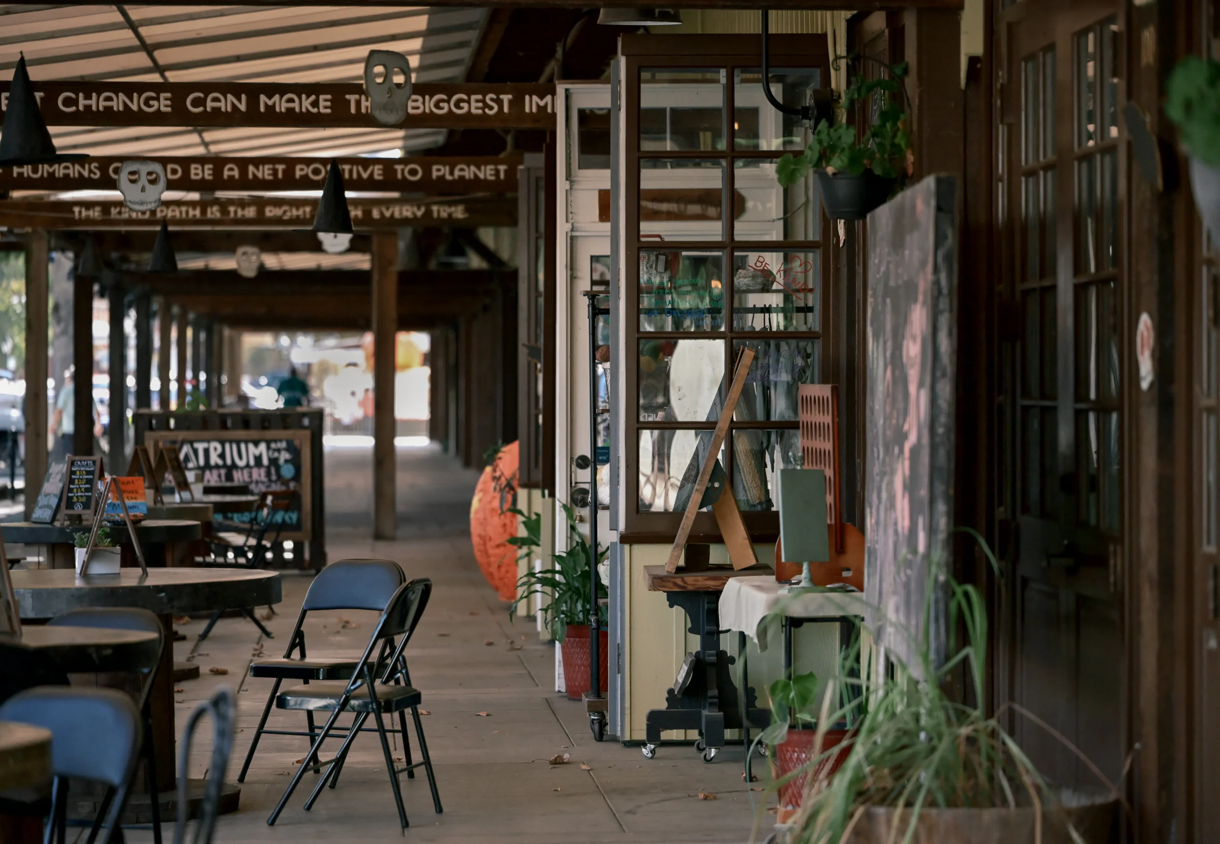 Tables, folding chairs and potted plants outside shops along a covered walkway
