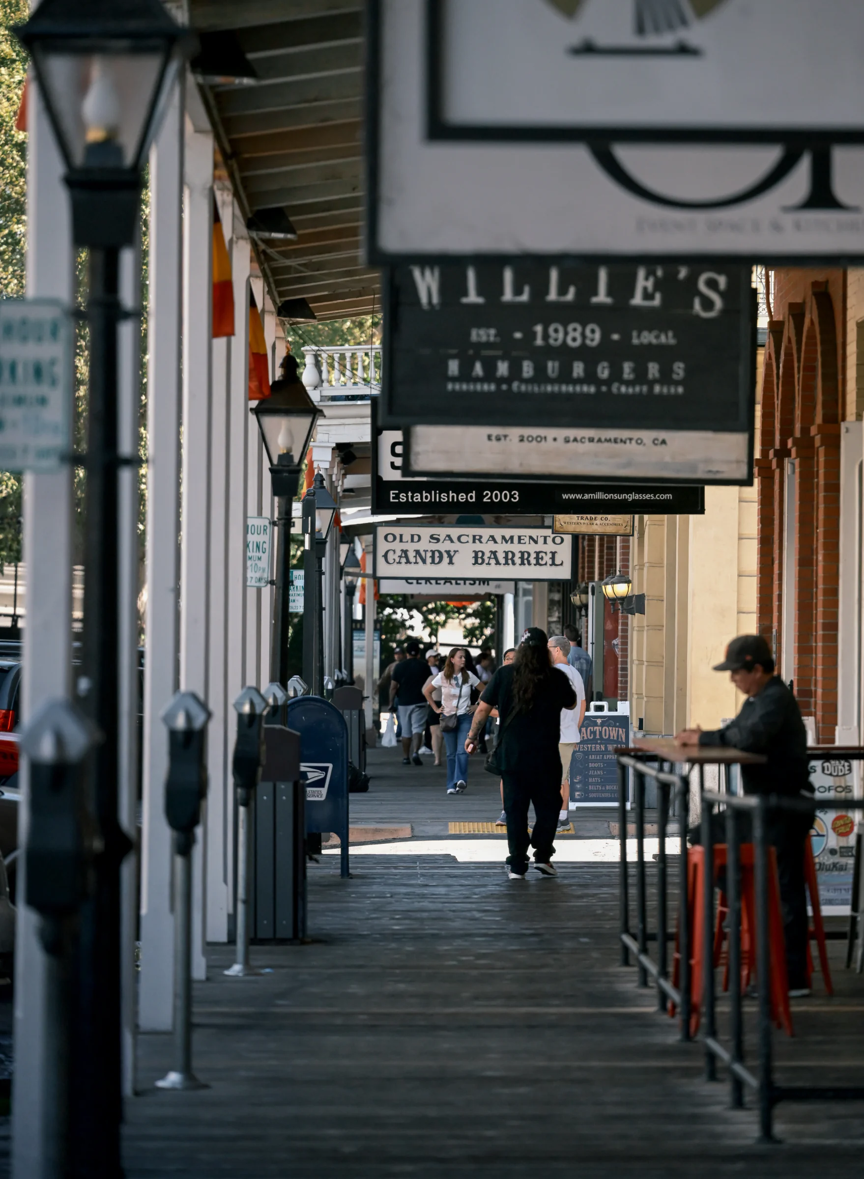 Pedestrians beneath overlapping shop signs between columns and brick storefronts