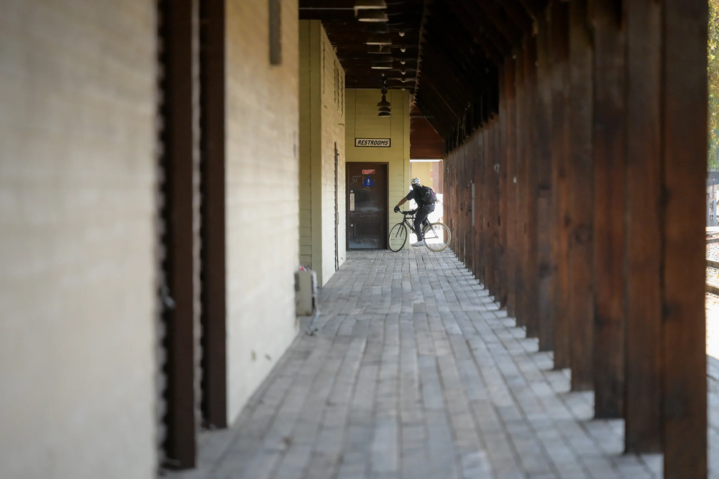 A cyclist at the far end of a wooden walkway lined with timber columns