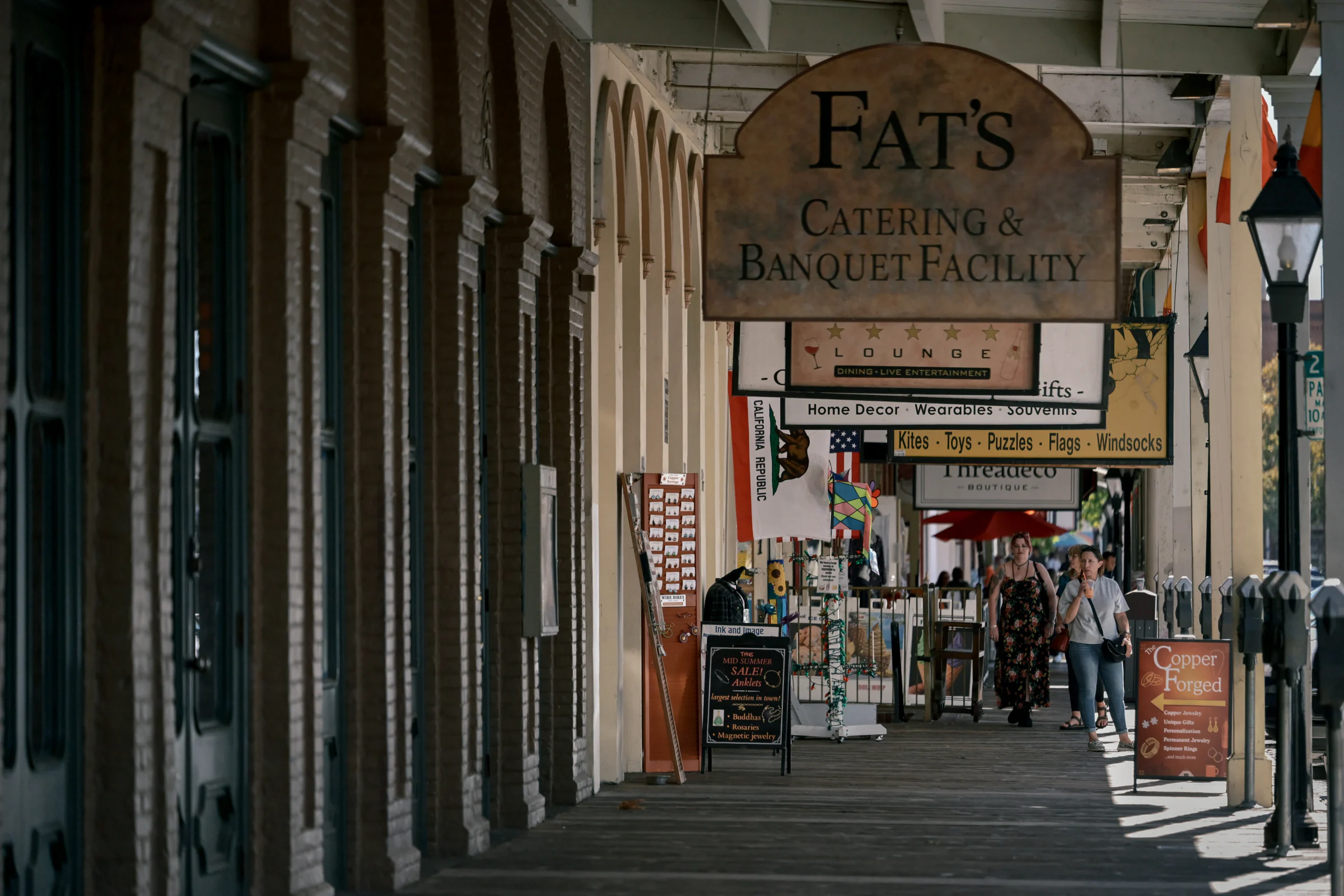 People walking beneath hanging signs beside arched storefronts and merchandise displays