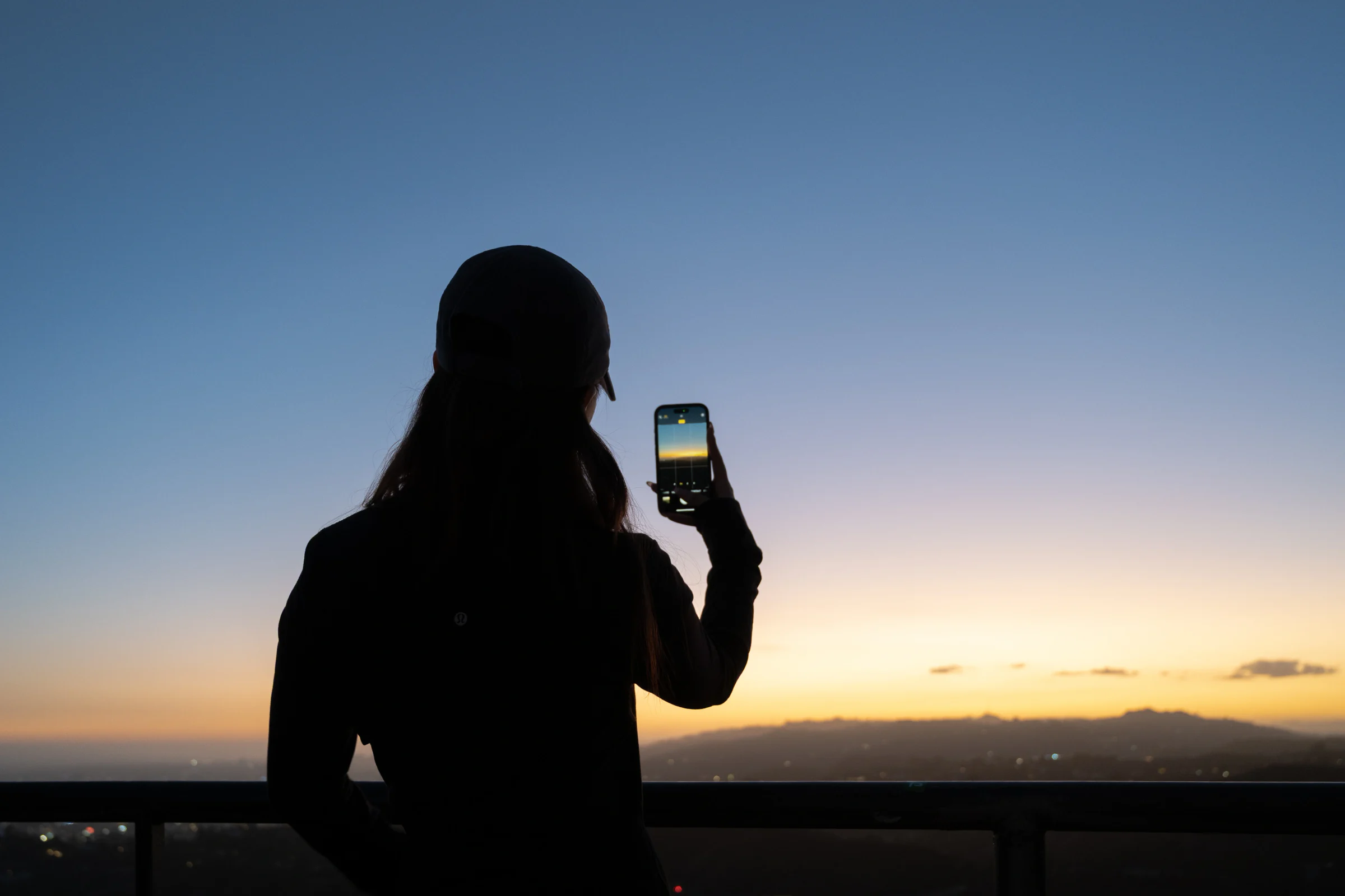 Silhouette of a person holding up a phone to photograph the horizon at dusk