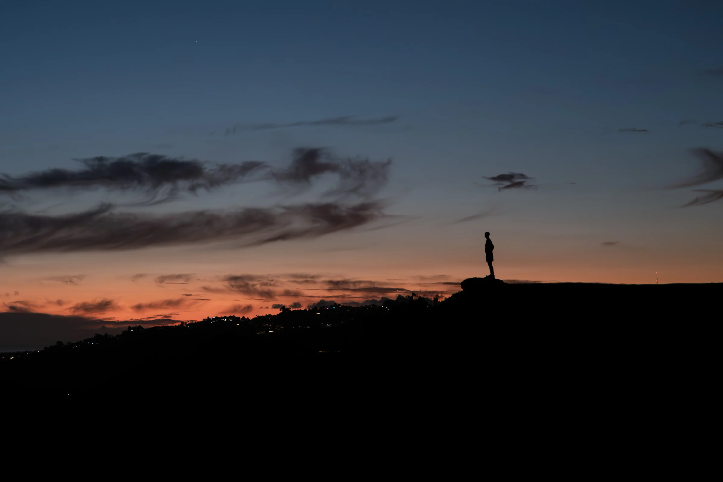 Distant silhouette standing on a ridge beneath clouds in the dusk sky
