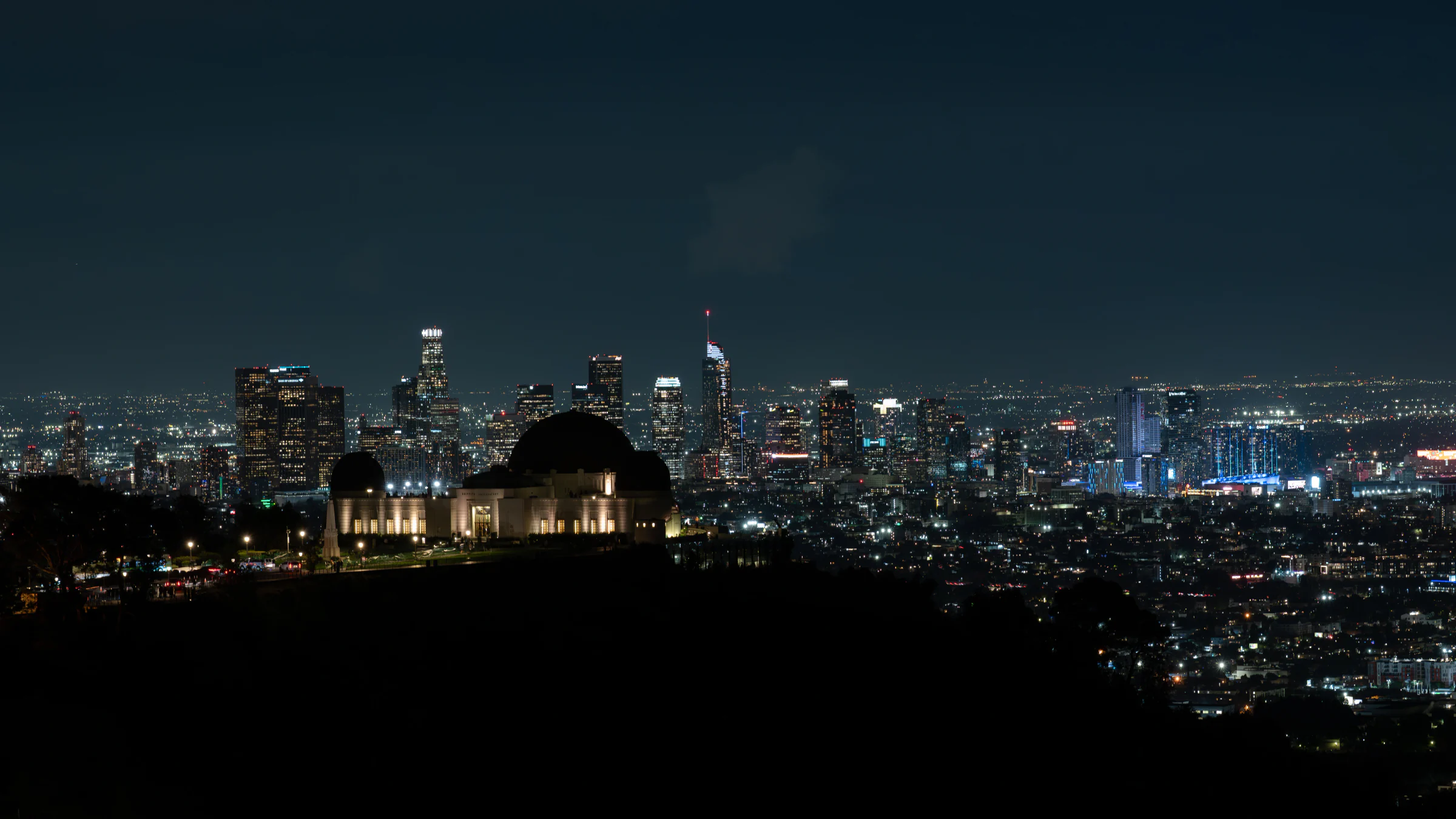 Griffith Observatory lit at night, with the downtown Los Angeles skyline beyond