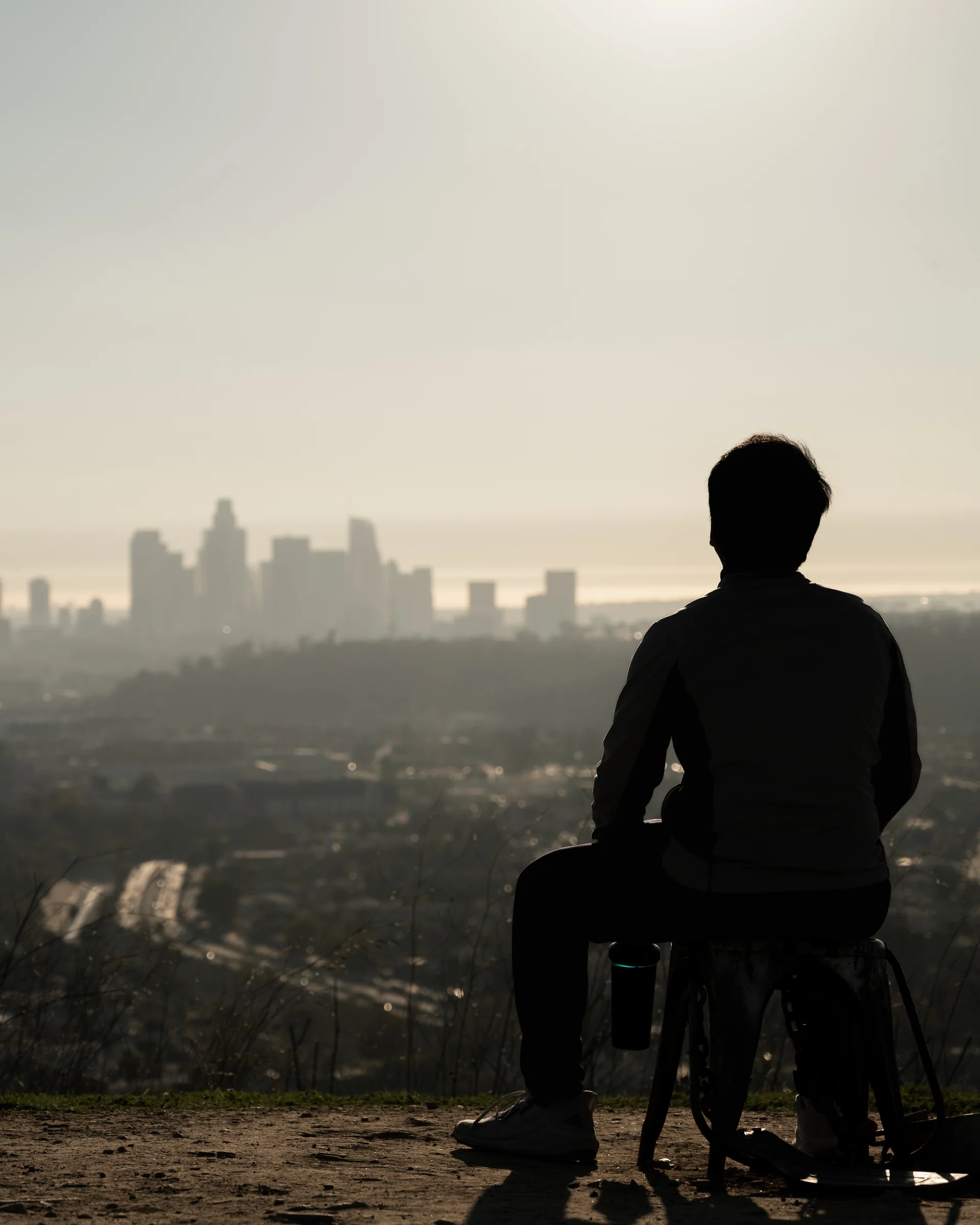 A seated person silhouetted against a hazy city skyline